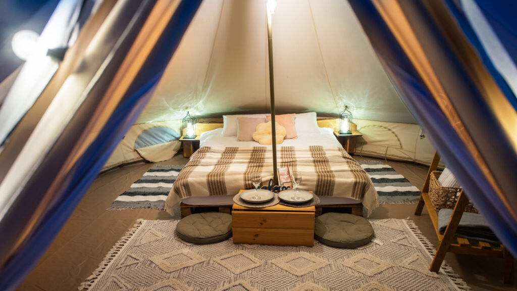 Tent interior with lamps, bed and furniture at glamping, night